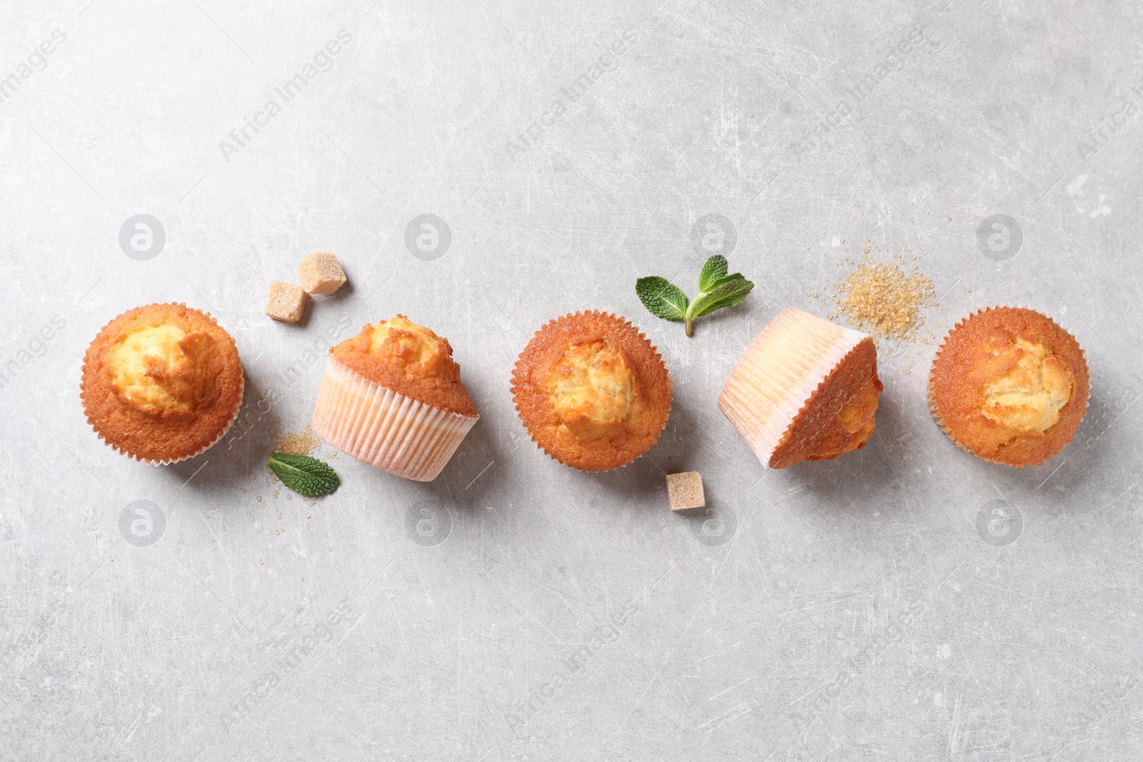 Photo of Delicious sweet muffins and brown sugar on light grey textured table, flat lay