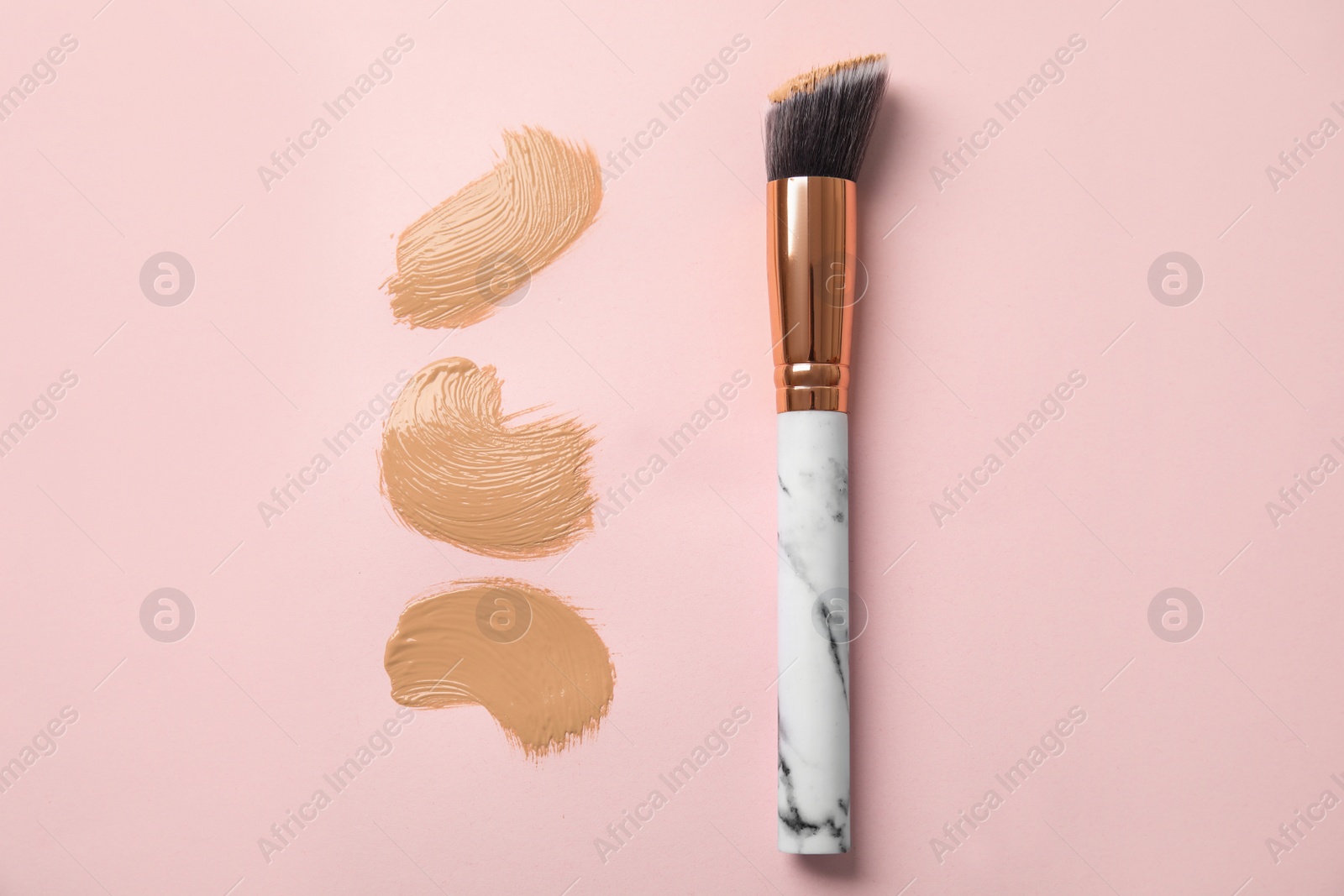 Photo of Samples of liquid foundation and makeup brush on pink background, top view