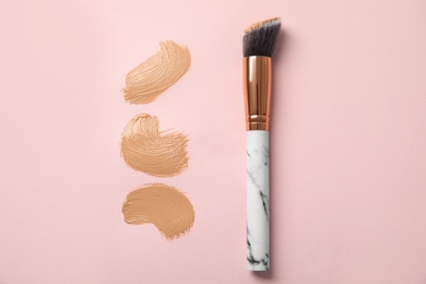 Samples of liquid foundation and makeup brush on pink background, top view