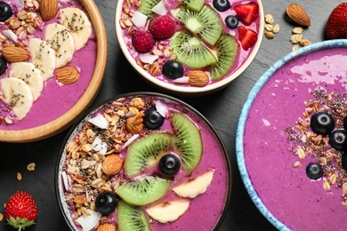Photo of Acai smoothie bowls with granola and fruits on black table, flat lay