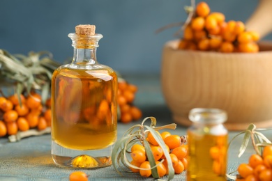 Photo of Natural sea buckthorn oil and fresh berries on blue wooden table