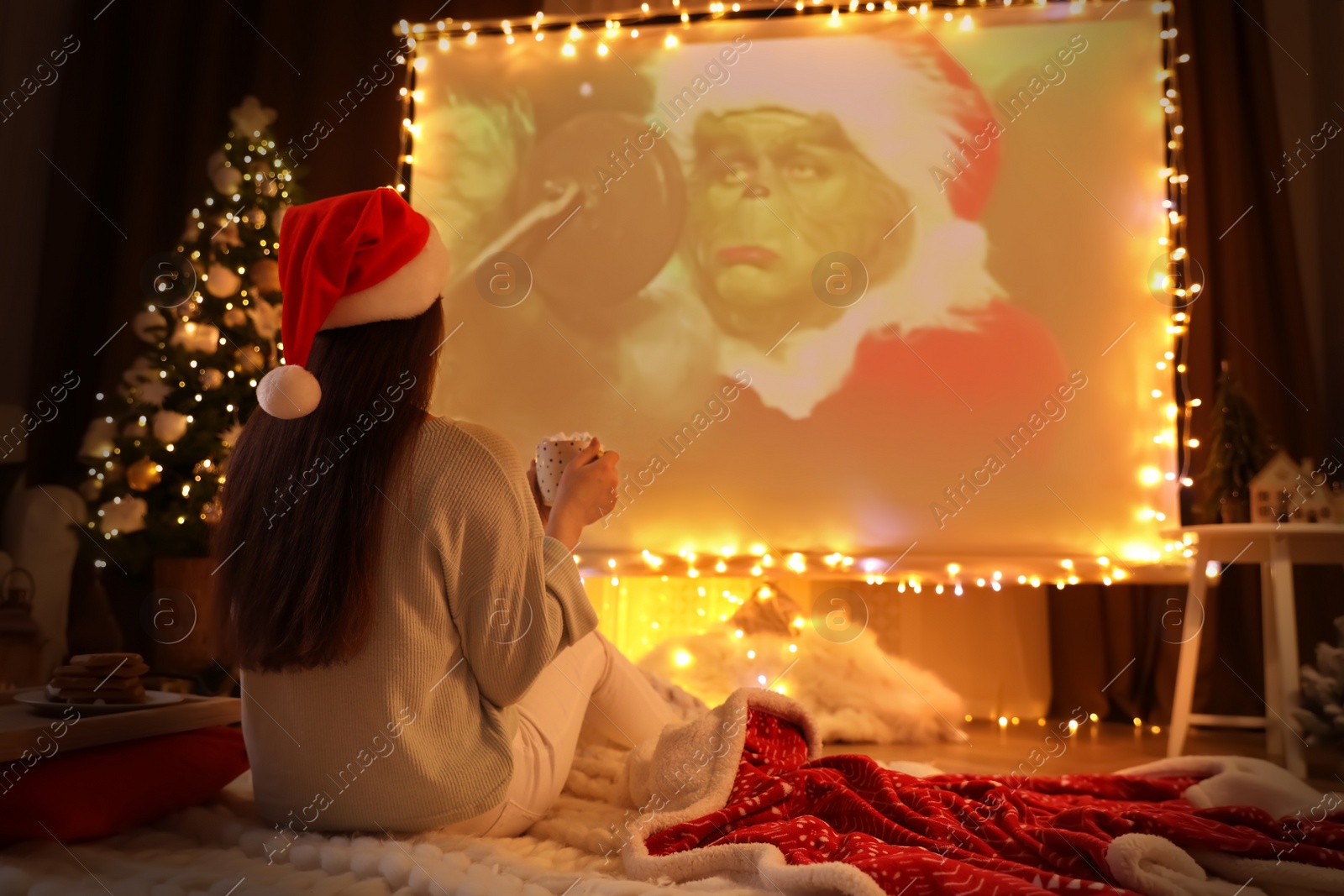 Photo of MYKOLAIV, UKRAINE - DECEMBER 24, 2020: Woman watching The Grinch movie via video projector in room. Cozy winter holidays atmosphere