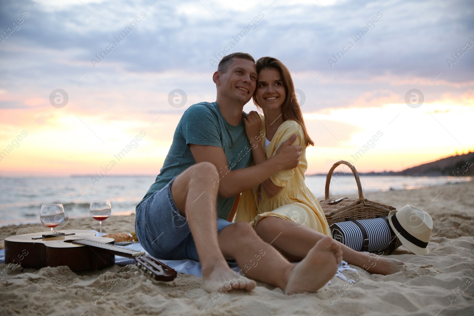 Photo of Lovely couple having romantic picnic on beach at sunset