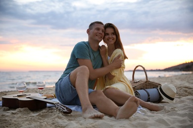 Photo of Lovely couple having romantic picnic on beach at sunset