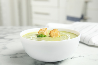 Photo of Delicious broccoli cream soup with croutons served on white marble table indoors