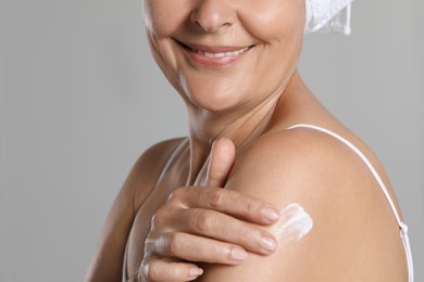 Photo of Happy woman applying body cream onto shoulder on light background, closeup