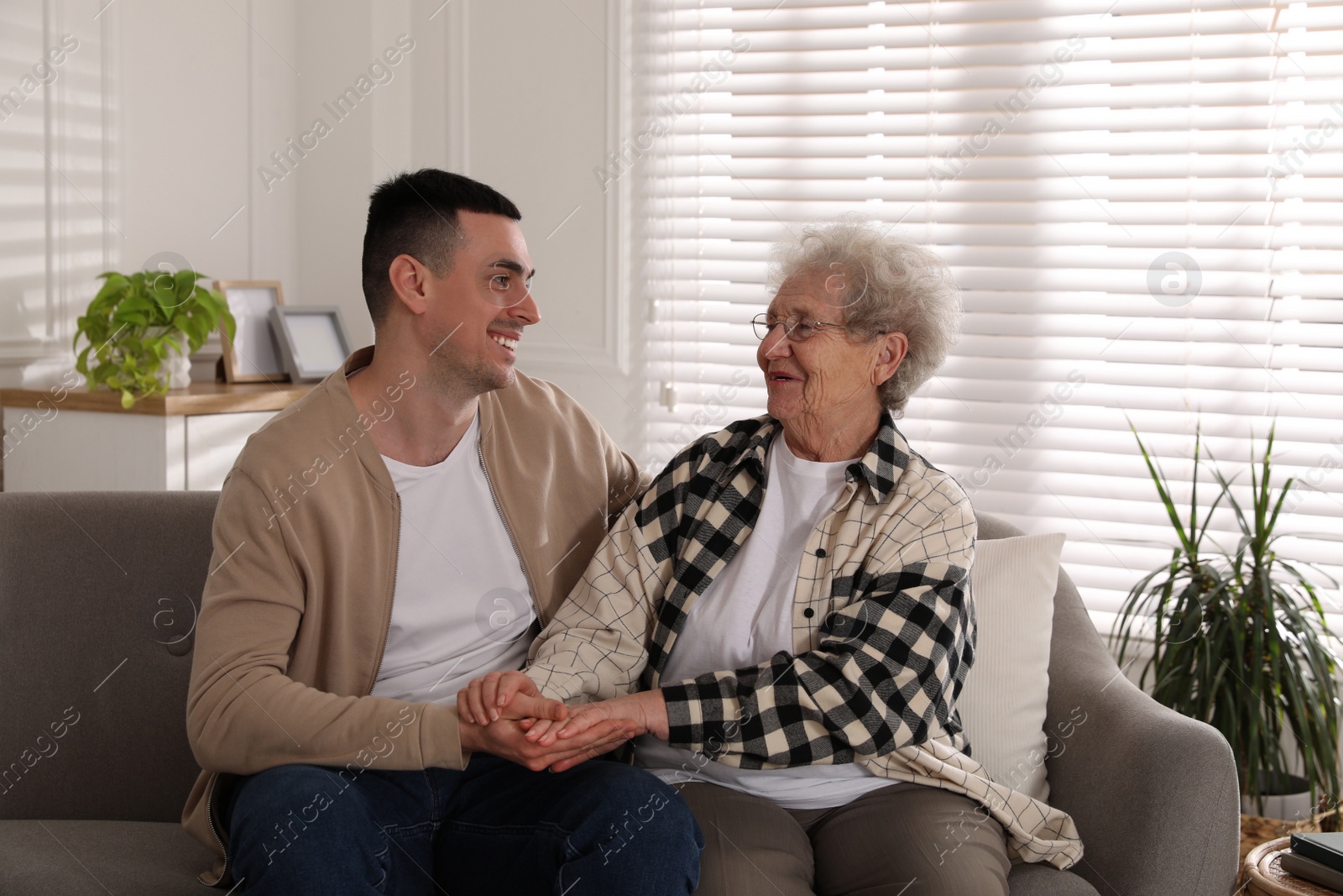 Photo of Young caregiver talking to senior woman in living room. Home health care service