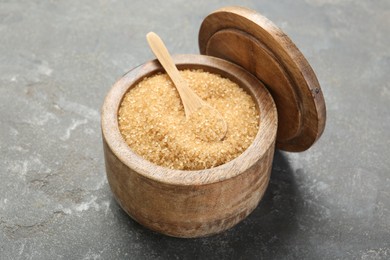 Photo of Brown sugar in bowl and spoon on grey textured table, closeup