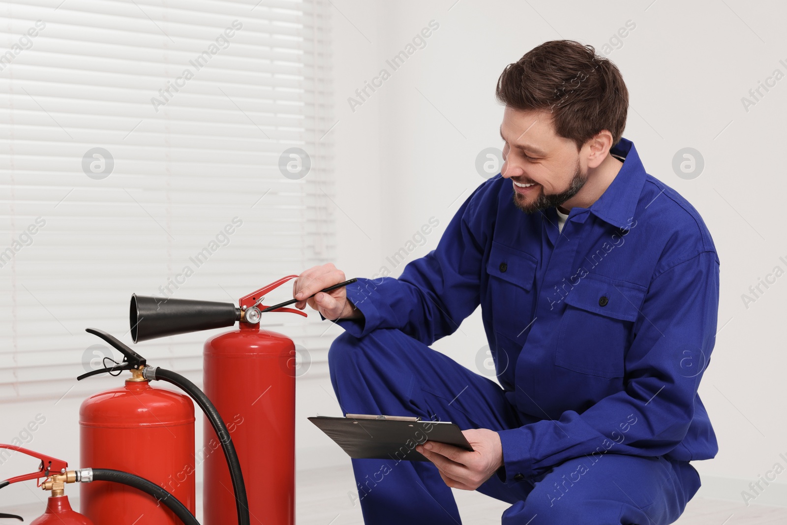 Photo of Man with clipboard checking fire extinguishers indoors