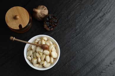 Garlic with honey in bowl and fermented black garlic on table, flat lay. Space for text
