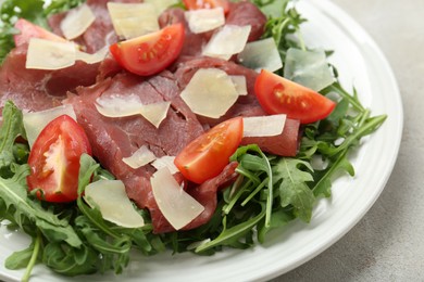 Photo of Delicious bresaola salad with parmesan cheese on light grey textured table, closeup