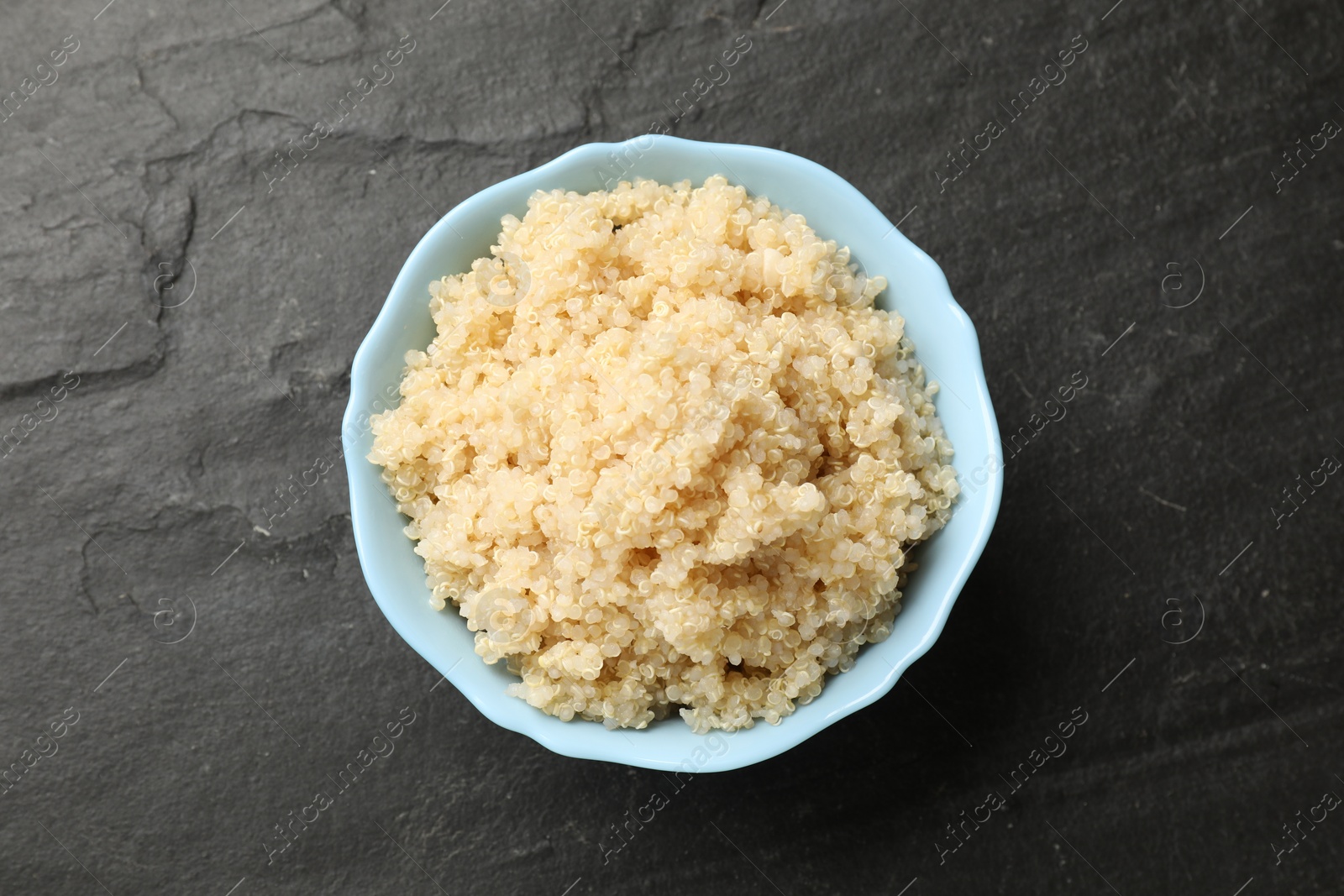 Photo of Tasty quinoa porridge in bowl on black textured table, top view