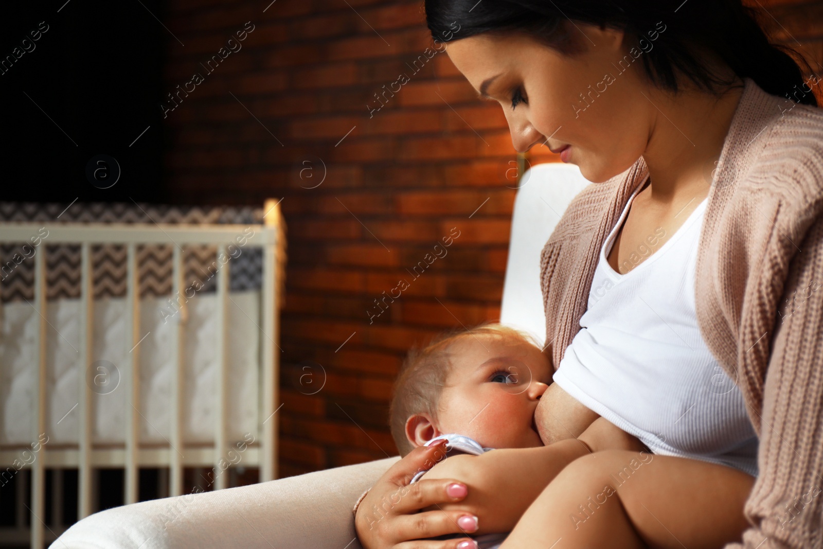 Photo of Woman breast feeding her baby in armchair at home, closeup