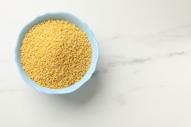 Photo of Millet groats in bowl on white marble table, top view. Space for text