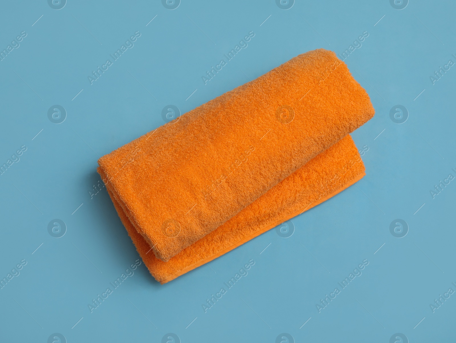 Photo of Rolled orange beach towel on light blue background, top view
