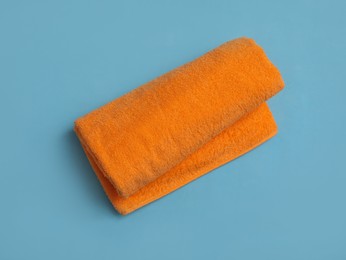 Rolled orange beach towel on light blue background, top view