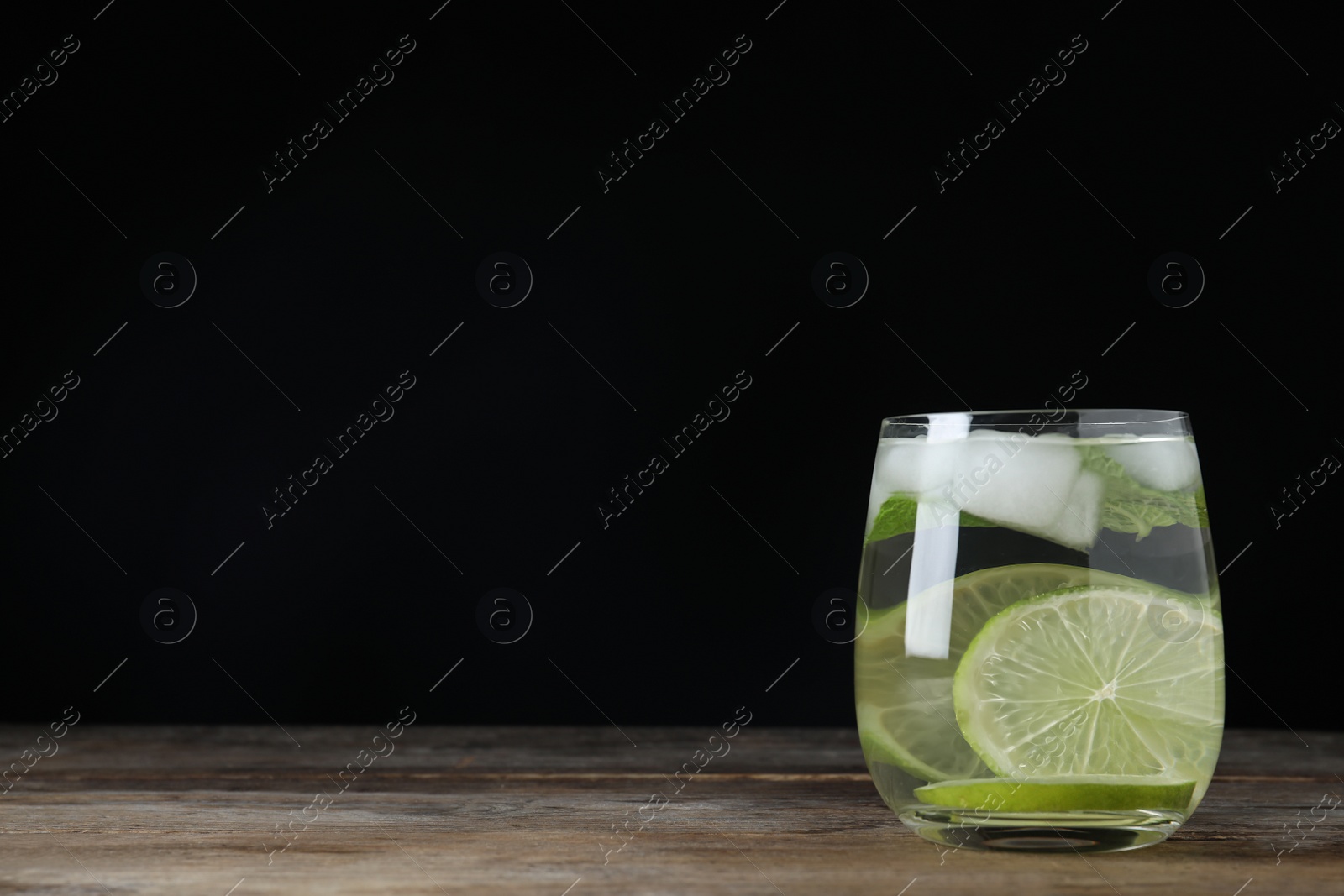 Photo of Vodka cocktail with lime and ice on wooden table against black background. Space for text