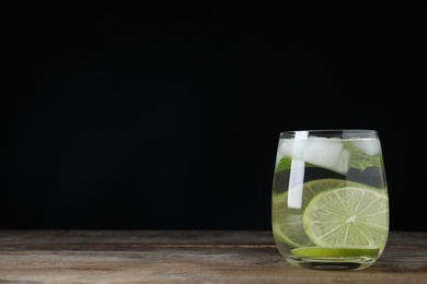 Vodka cocktail with lime and ice on wooden table against black background. Space for text