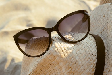Photo of Hat with beautiful sunglasses on sandy beach, closeup