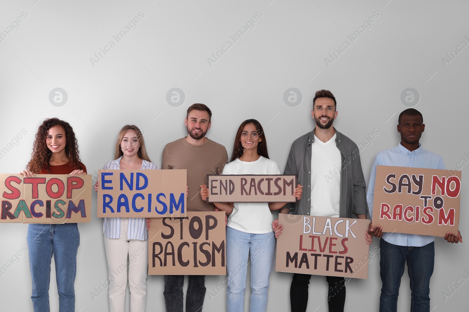 Photo of Protesters demonstrating different anti racism slogans on light background. People holding signs with phrases