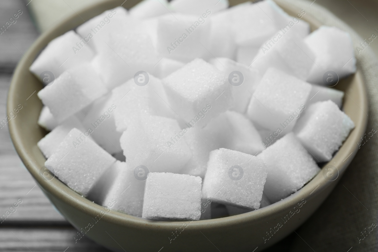 Photo of White sugar cubes in bowl on wooden table, closeup