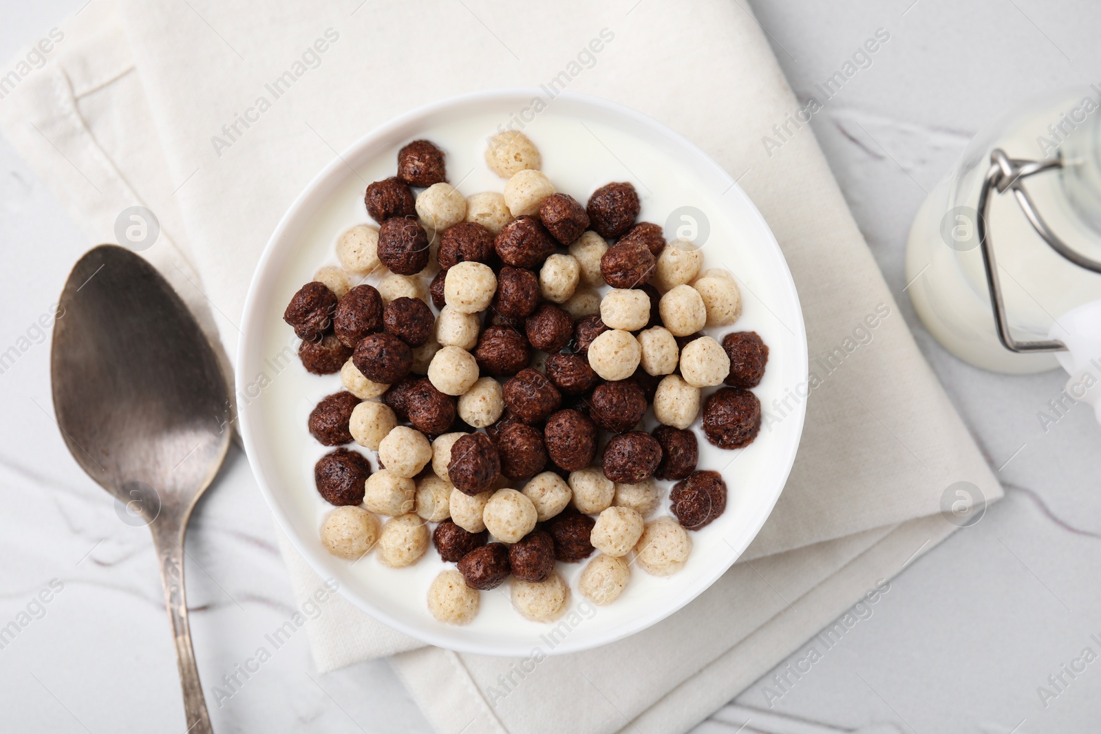 Photo of Breakfast cereal. Tasty corn balls with milk in bowl and spoon on white textured table, top view