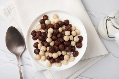 Breakfast cereal. Tasty corn balls with milk in bowl and spoon on white textured table, top view