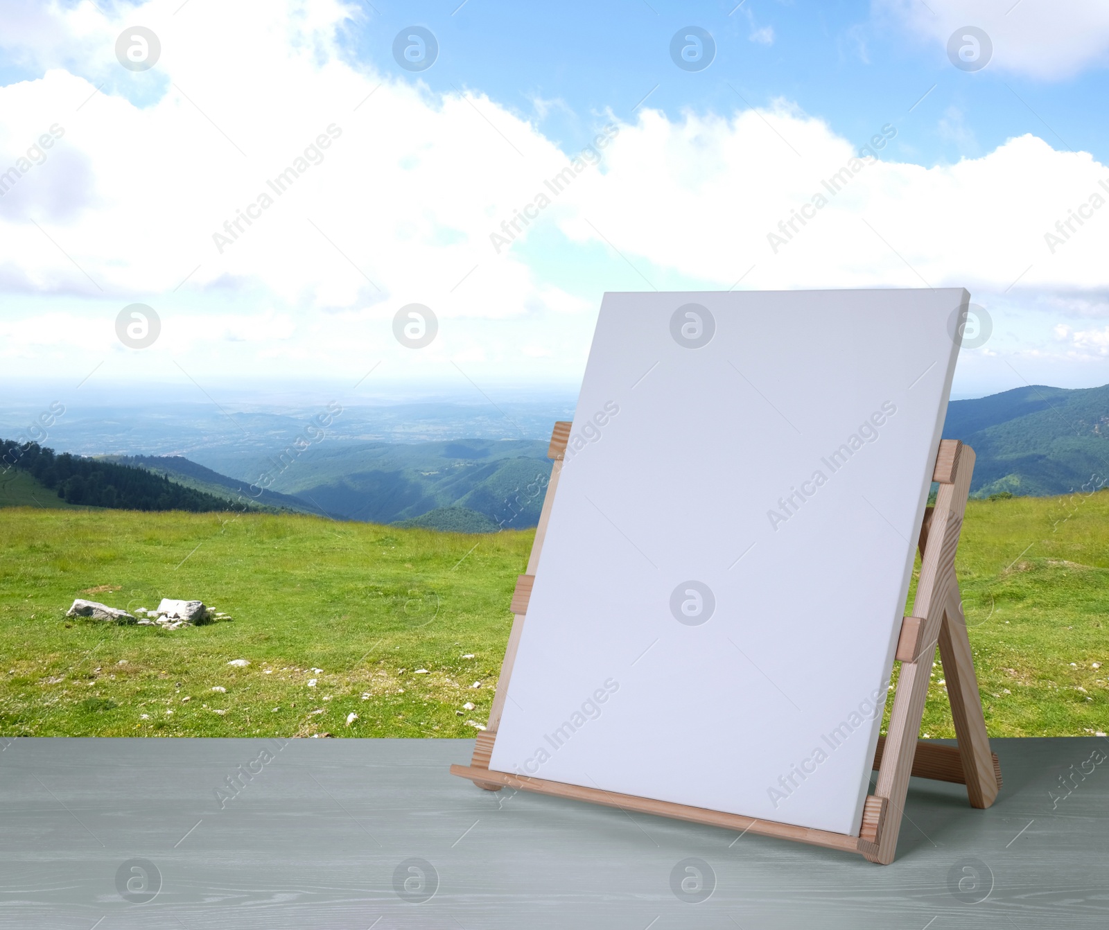 Image of Wooden easel with blank canvas on table and beautiful mountain landscape. Space for text