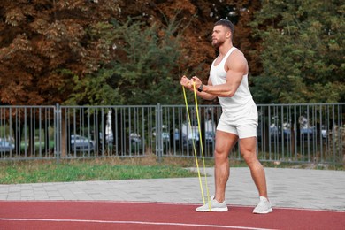 Muscular man doing exercise with elastic resistance band outdoors