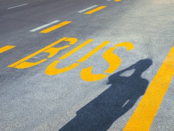 Bus stop pad and man's shadow on asphalt road