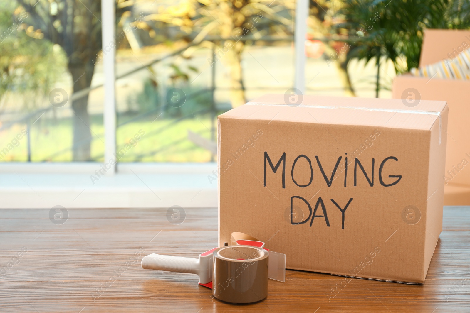 Photo of Cardboard box with words MOVING DAY and packaging items on wooden table