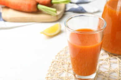 Photo of Glass of fresh carrot juice on white wooden table, space for text