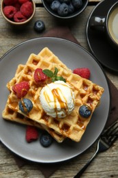 Photo of Delicious Belgian waffles with ice cream, berries and caramel sauce served on wooden table, flat lay