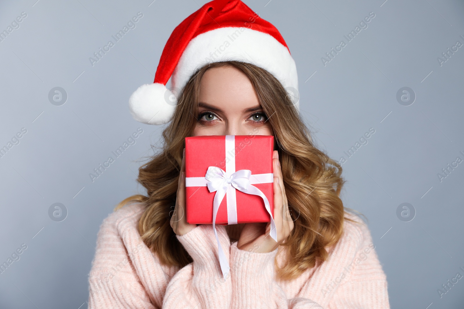 Photo of Happy young woman wearing Santa hat with Christmas gift on grey background