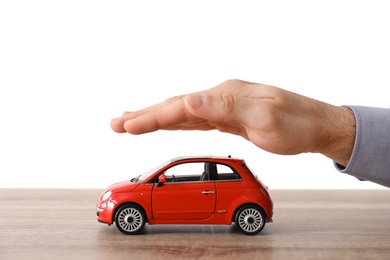 Photo of Male insurance agent covering toy car at table, closeup