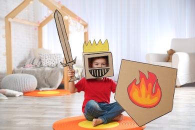 Cute little boy playing with cardboard armor in bedroom