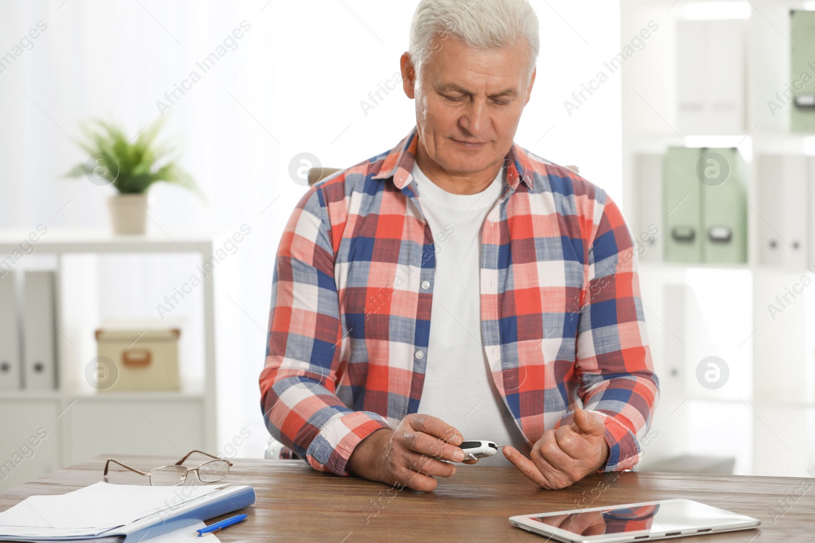 Photo of Senior man using digital glucometer at table. Diabetes control