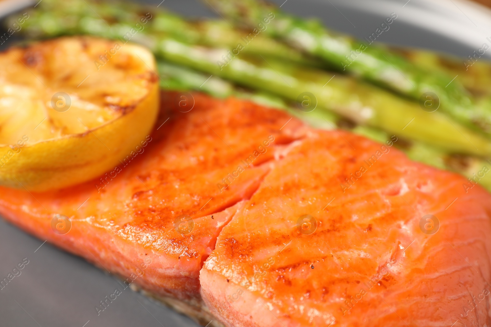 Photo of Tasty grilled salmon with asparagus and lemon on grey plate, closeup