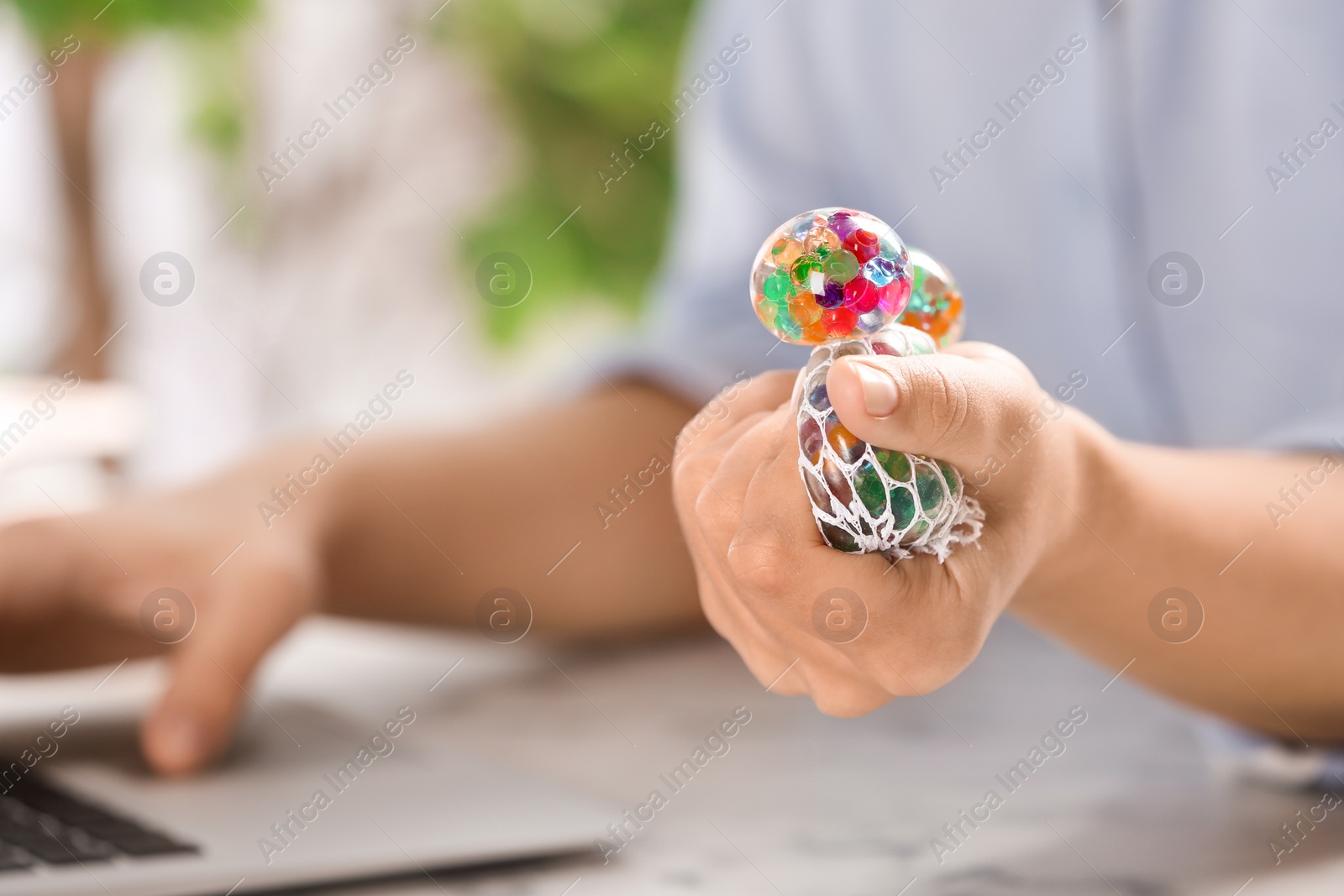 Photo of Woman squeezing colorful slime in office, closeup. Antistress toy