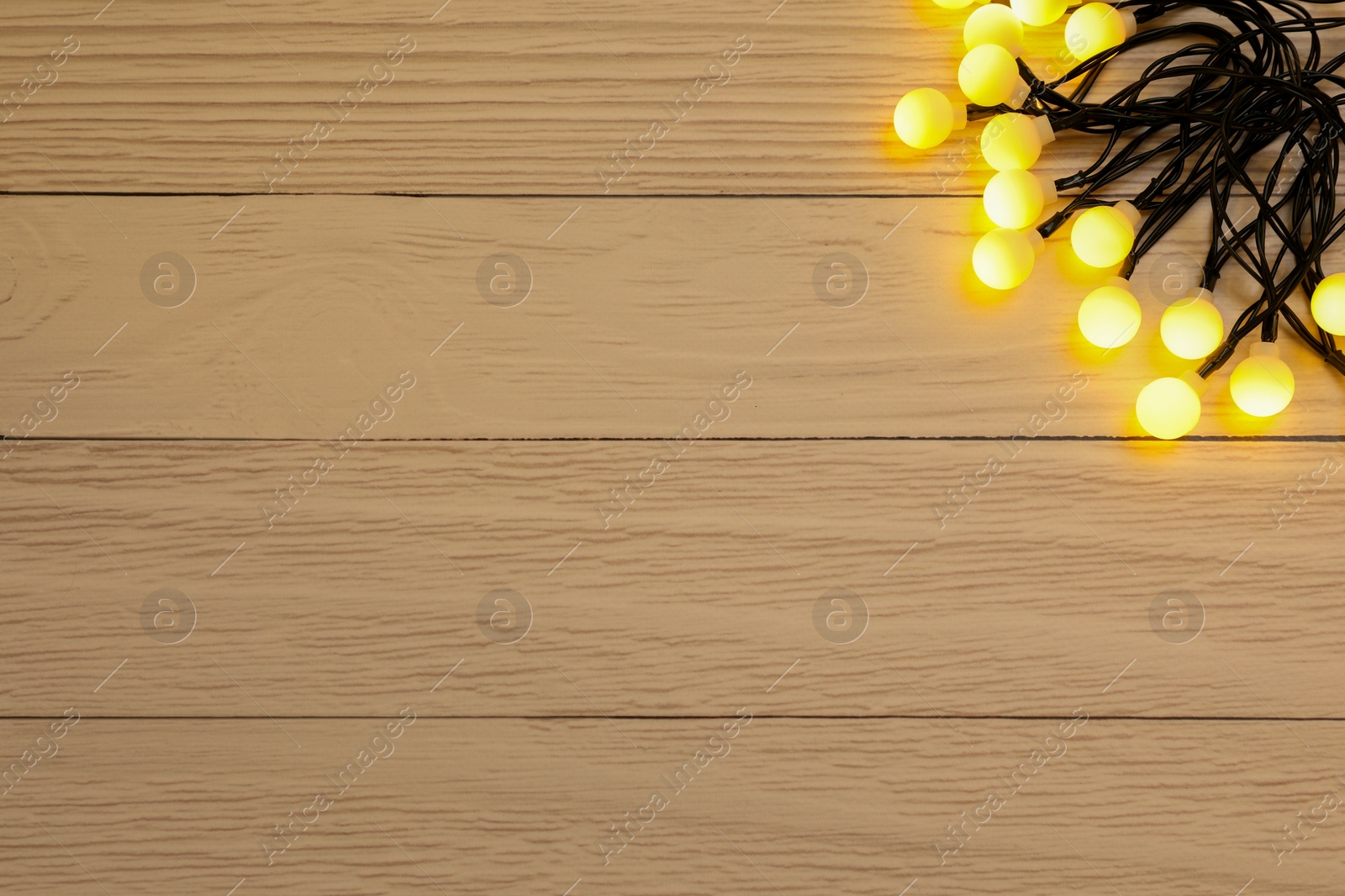 Photo of Glowing festive lights on wooden background, top view. Space for text