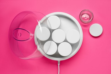 Modern yogurt maker with jars on pink background, flat lay