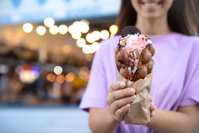 Young woman holding delicious sweet bubble waffle with ice cream outdoors, closeup