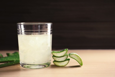 Glass of aloe vera juice and green leaves on wooden table against dark background with space for text