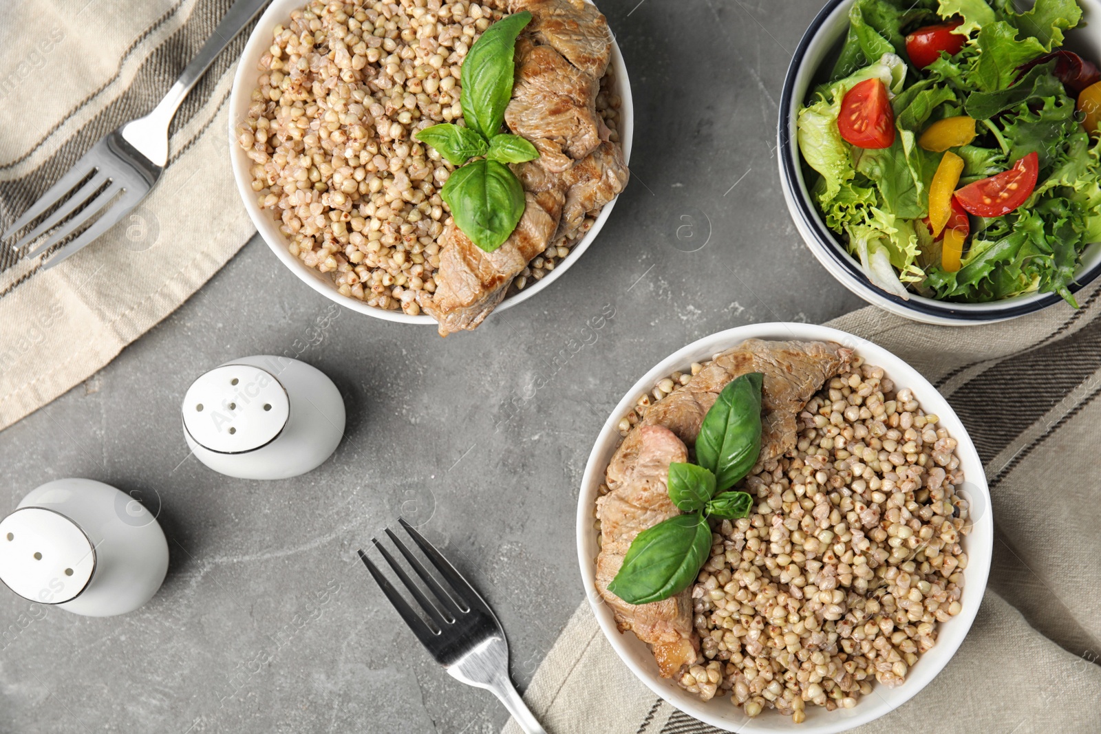 Photo of Tasty buckwheat porridge with meat on grey table, flat lay