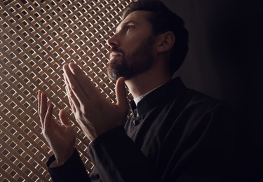 Photo of Catholic priest in cassock praying to God in confessional booth