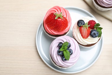 Photo of Sweet cupcakes with fresh berries on light wooden table, flat lay. Space for text