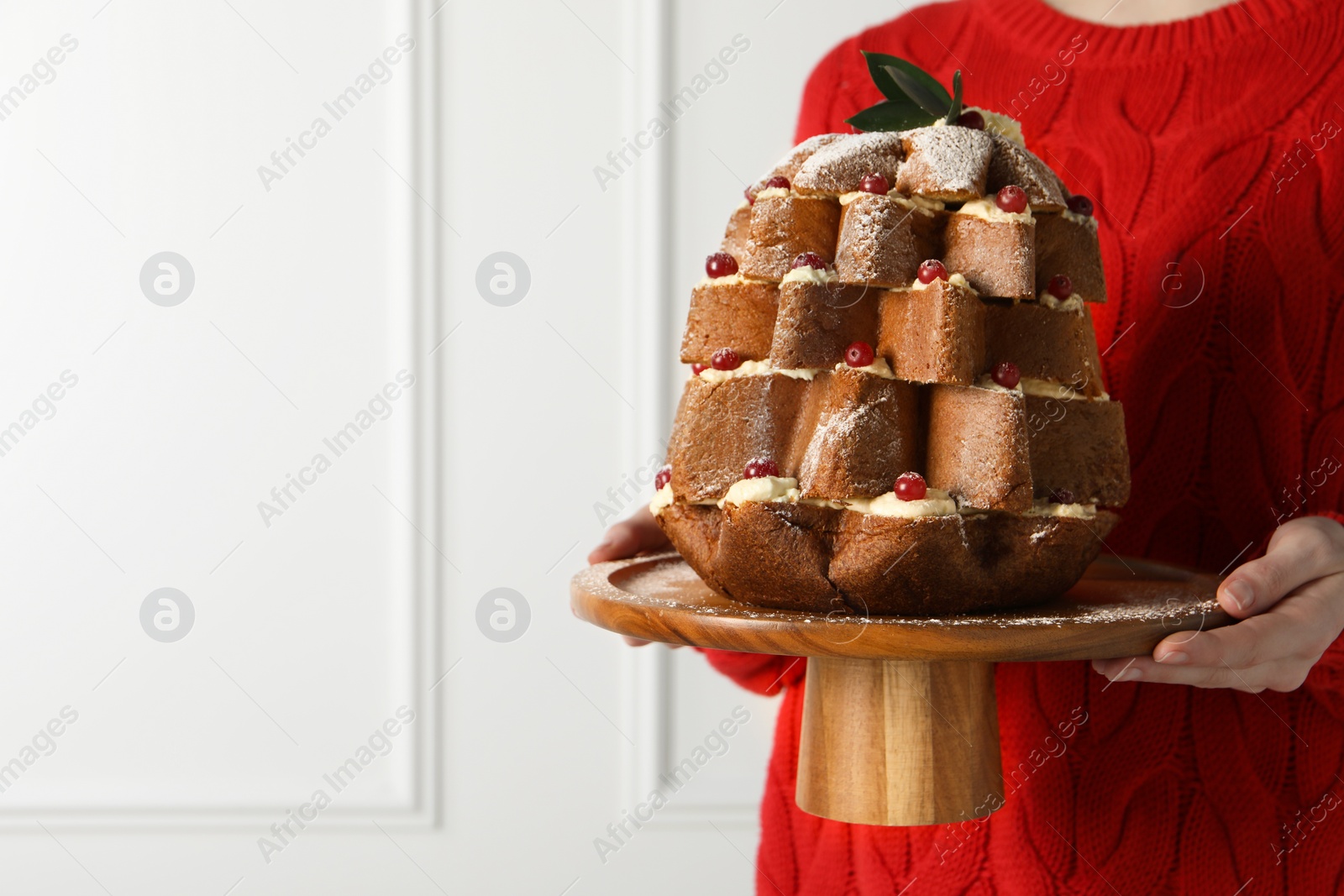 Photo of Woman holding delicious Pandoro Christmas tree cake decorated with powdered sugar and berries indoors, closeup. Space for text