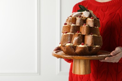 Photo of Woman holding delicious Pandoro Christmas tree cake decorated with powdered sugar and berries indoors, closeup. Space for text