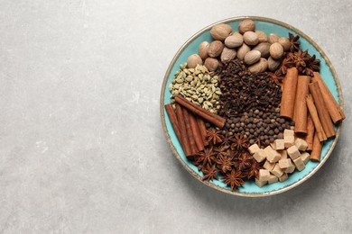 Photo of Different spices and nuts in bowl on light gray textured table, top view. Space for text