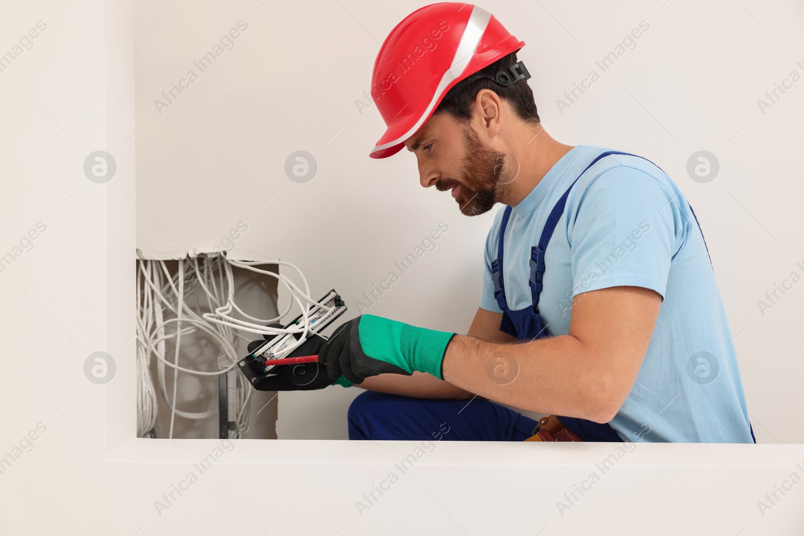 Photo of Electrician with screwdriver fixing patch panel indoors